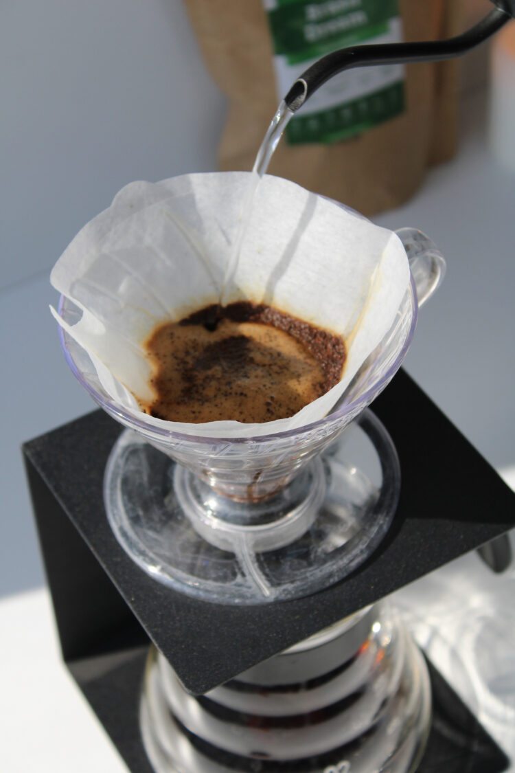 A ceramic V60 dripper with a paper filter and a cup of coffee beside it on a wooden table.